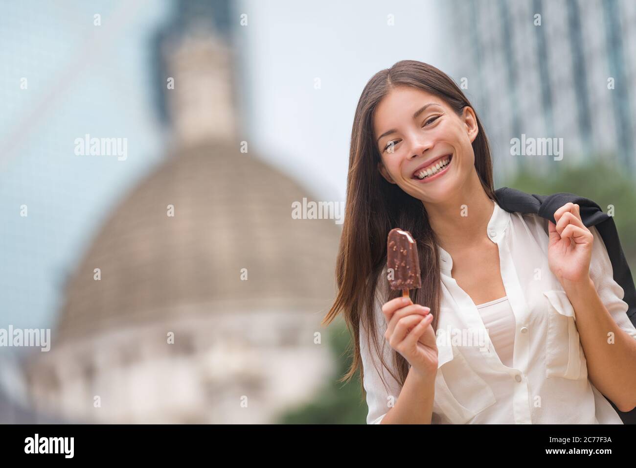 Business woman eating ice cream in Hong Kong. Young businesswoman enjoying ice-cream on at stick walking outside smiling happy in central Hong Kong Stock Photo