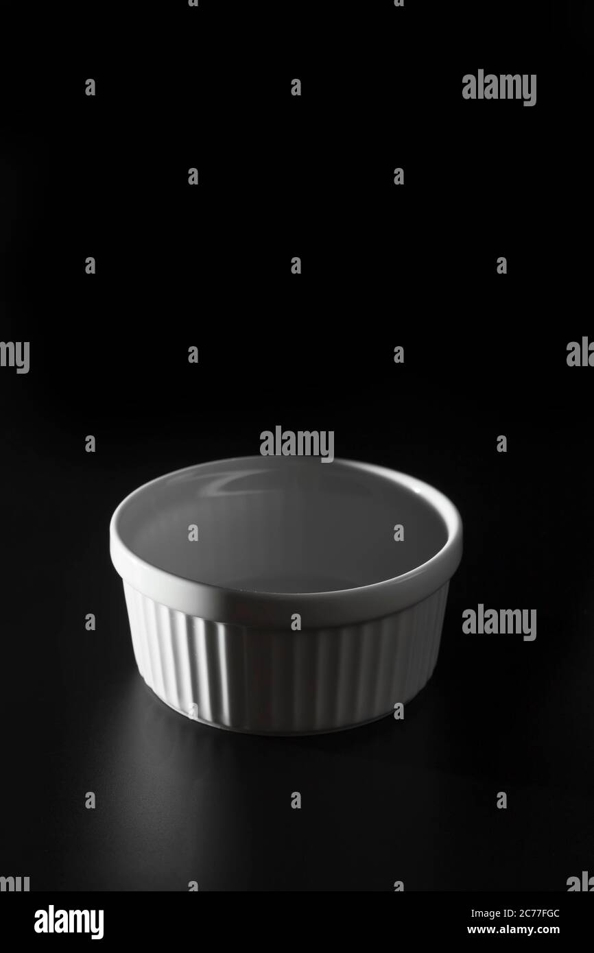 Empty white Ramekin on black background with copy space. Stock Photo