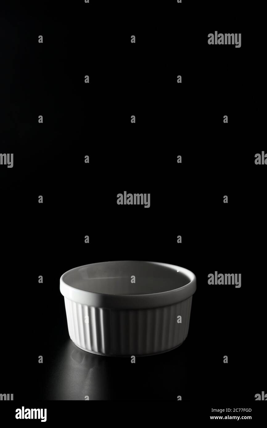 Empty white Ramekin on black background with copy space. Stock Photo