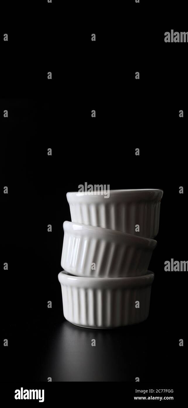 White ramekins stacked on black background with copy space. Stock Photo