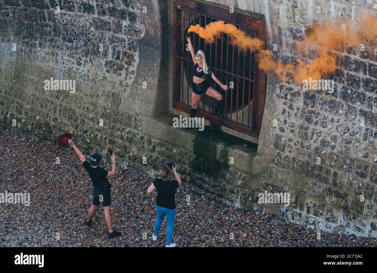Photographer and assistant shooting a woman setting off an orange smoke bomb against an urban background Stock Photo