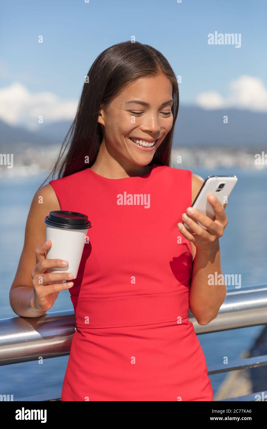 Happy Asian business woman on coffee break smiling texting sms message mobile data phone or reading online. City urban businesspeople lifestyle Stock Photo