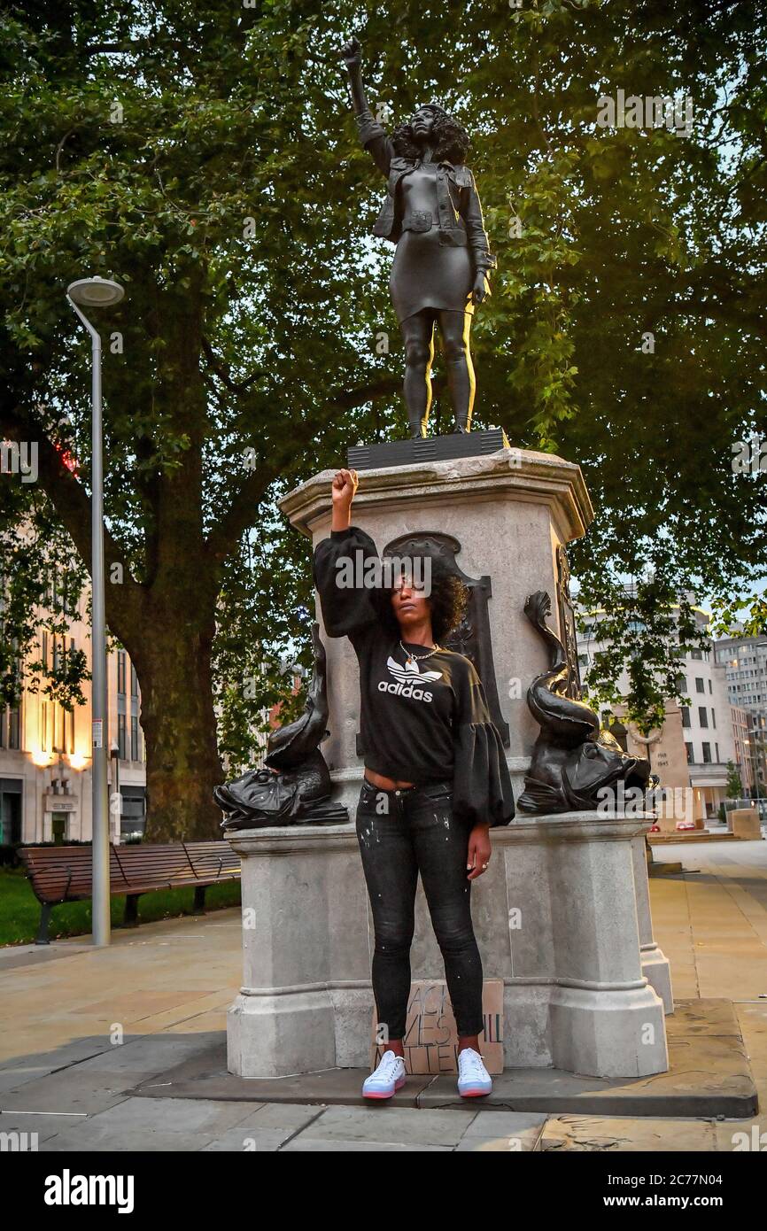 Jen Reid poses in front of her black resin and steel statue titled A Surge of Power (Jen Reid) 2020, by Marc Quinn, where it is installed on the vacant Edward Colston plinth in Bristol city centre. Stock Photo