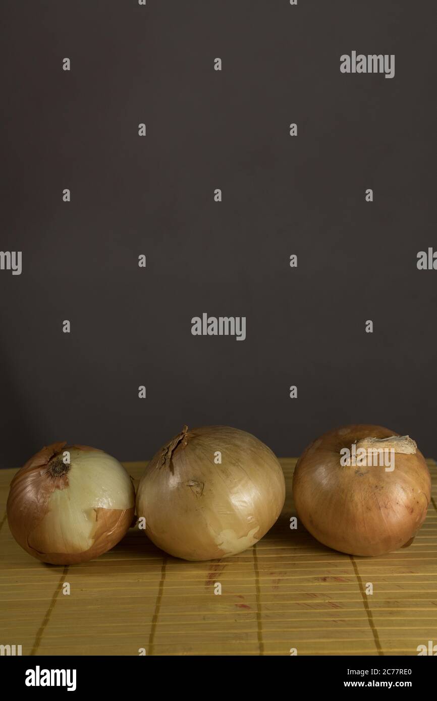 Three onions on board cutting, brown background Stock Photo