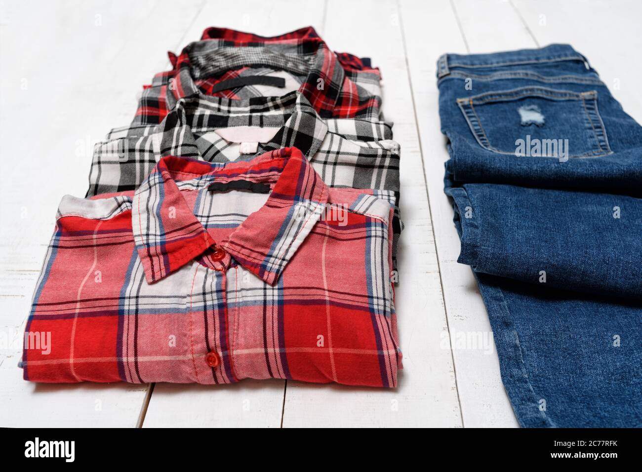 Four plaid shirts and blue jeans on a white wooden background. Clothing