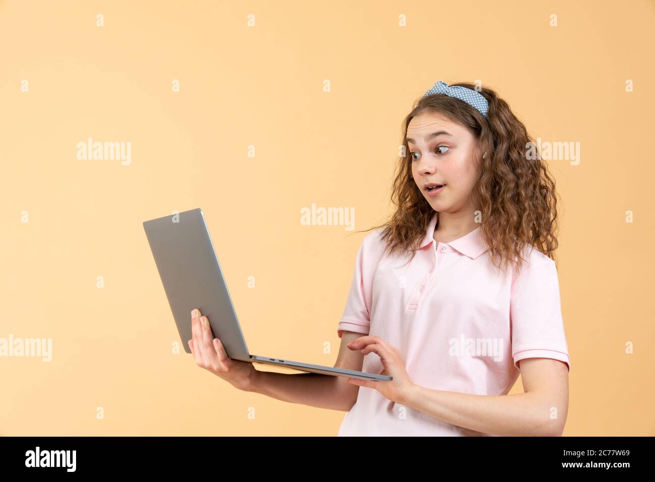 Portrait of frustrated computer user, teen girl with curly brunette hair in pink shirt looking at laptop, worried about software error, program bug Stock Photo