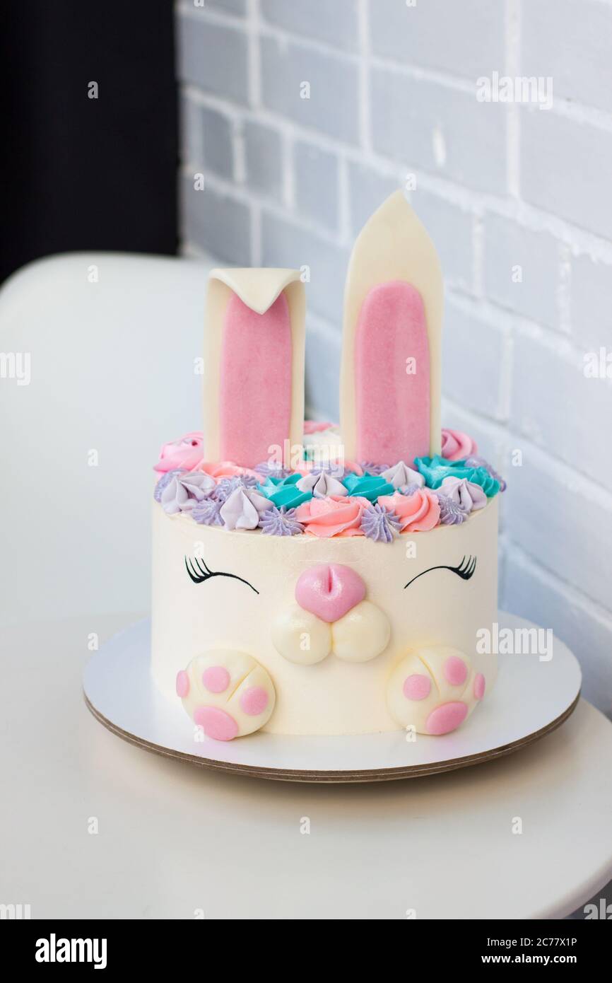 White and pink cake with cute bunny for children's birthday. Bunny made of fondant and buttercream. White background. Stock Photo