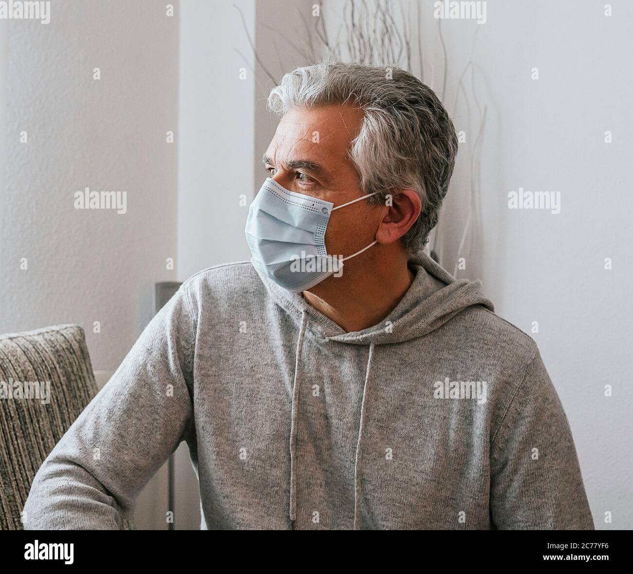 Older white-haired man wearing a mask against Coronavirus, Covid - 19 or any other disease, at home Stock Photo