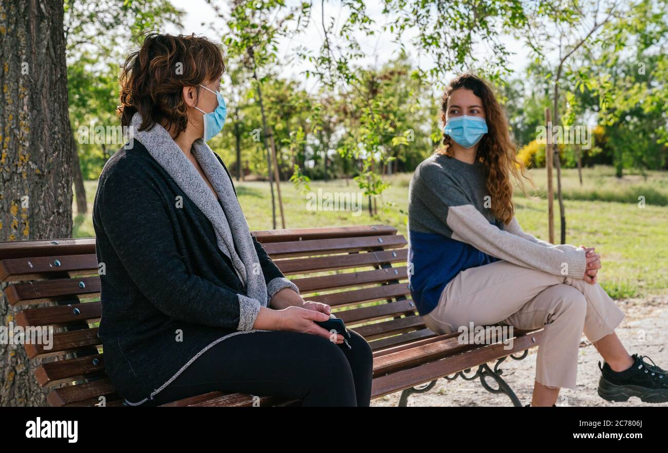 Social distance. Mother and daughter in social distancing sitting on bench in park. Pandemic. Coronavirus Stock Photo