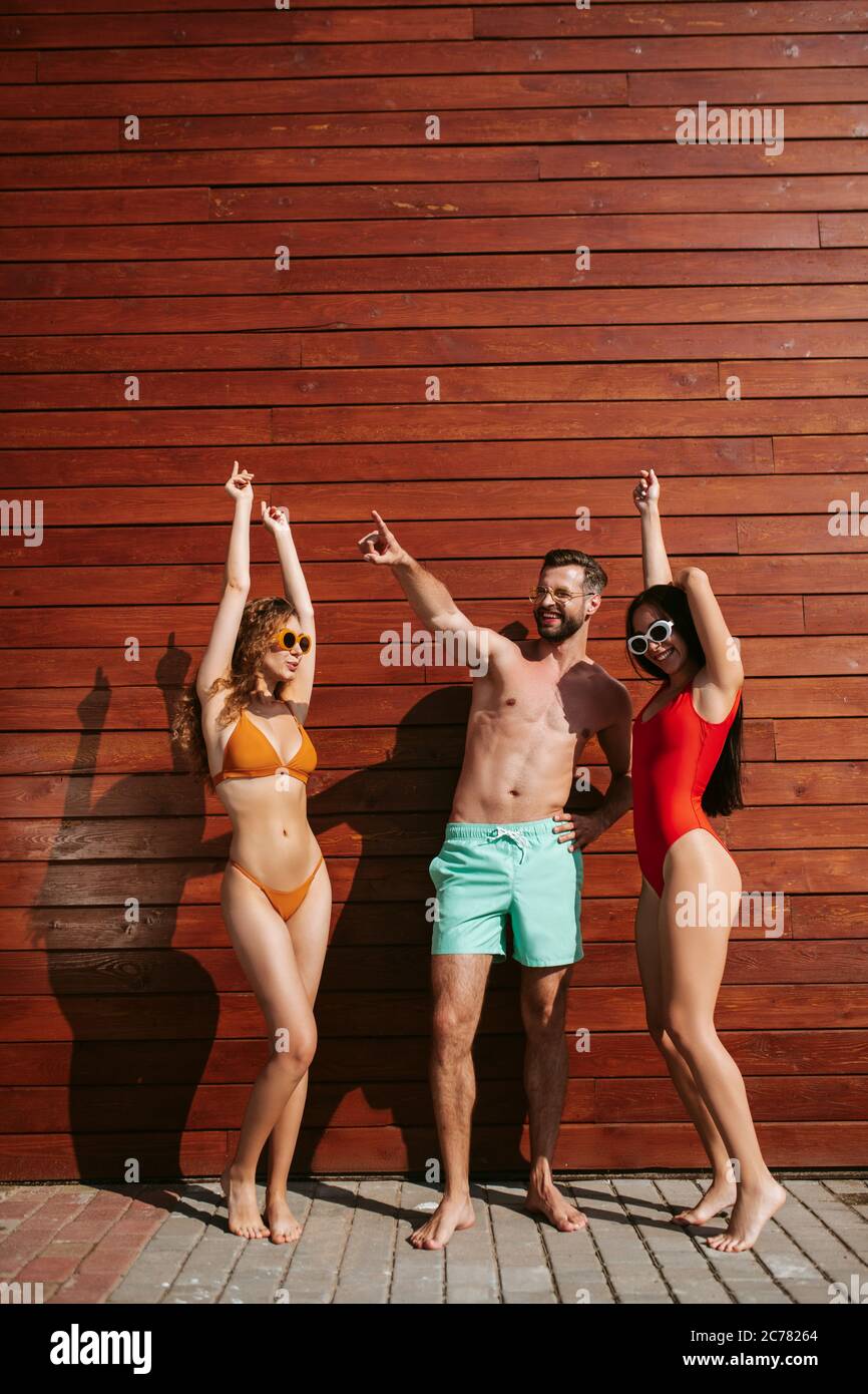three-young-friends-in-swimsuits-sunbathing-and-chatting-under-the-sun