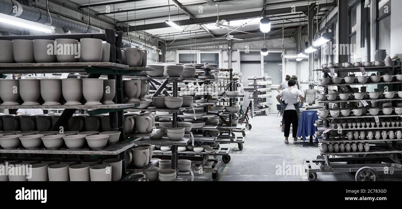 Boleslawiec, Lower Silesia, Poland., Shelves in a busy pottery studio full of finished work and clay pieces drying under the control of a woman Stock Photo