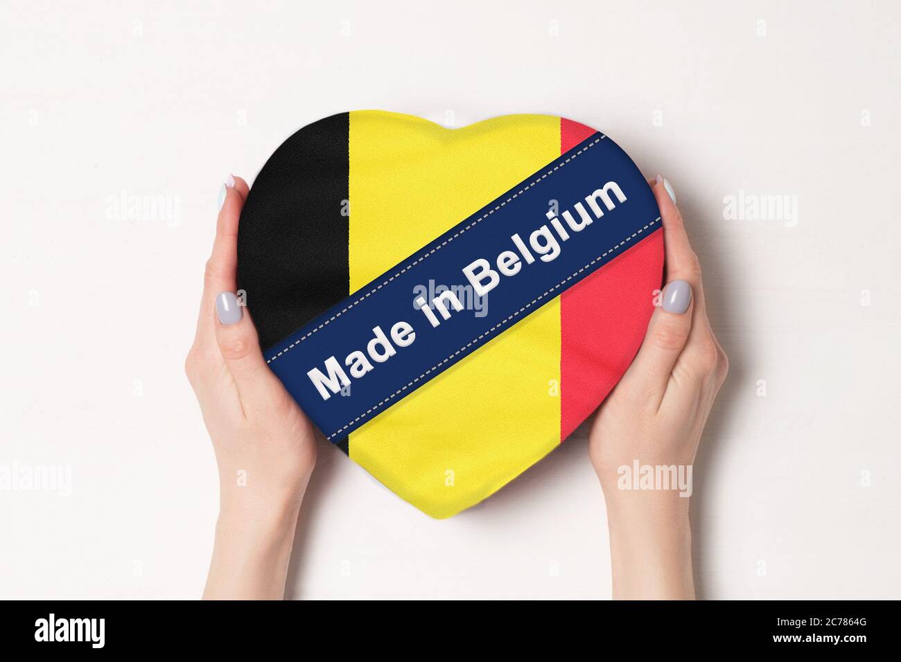 Inscription Made in Belgium, the flag of Belgium. Female hands holding a heart shaped box. White background. Stock Photo