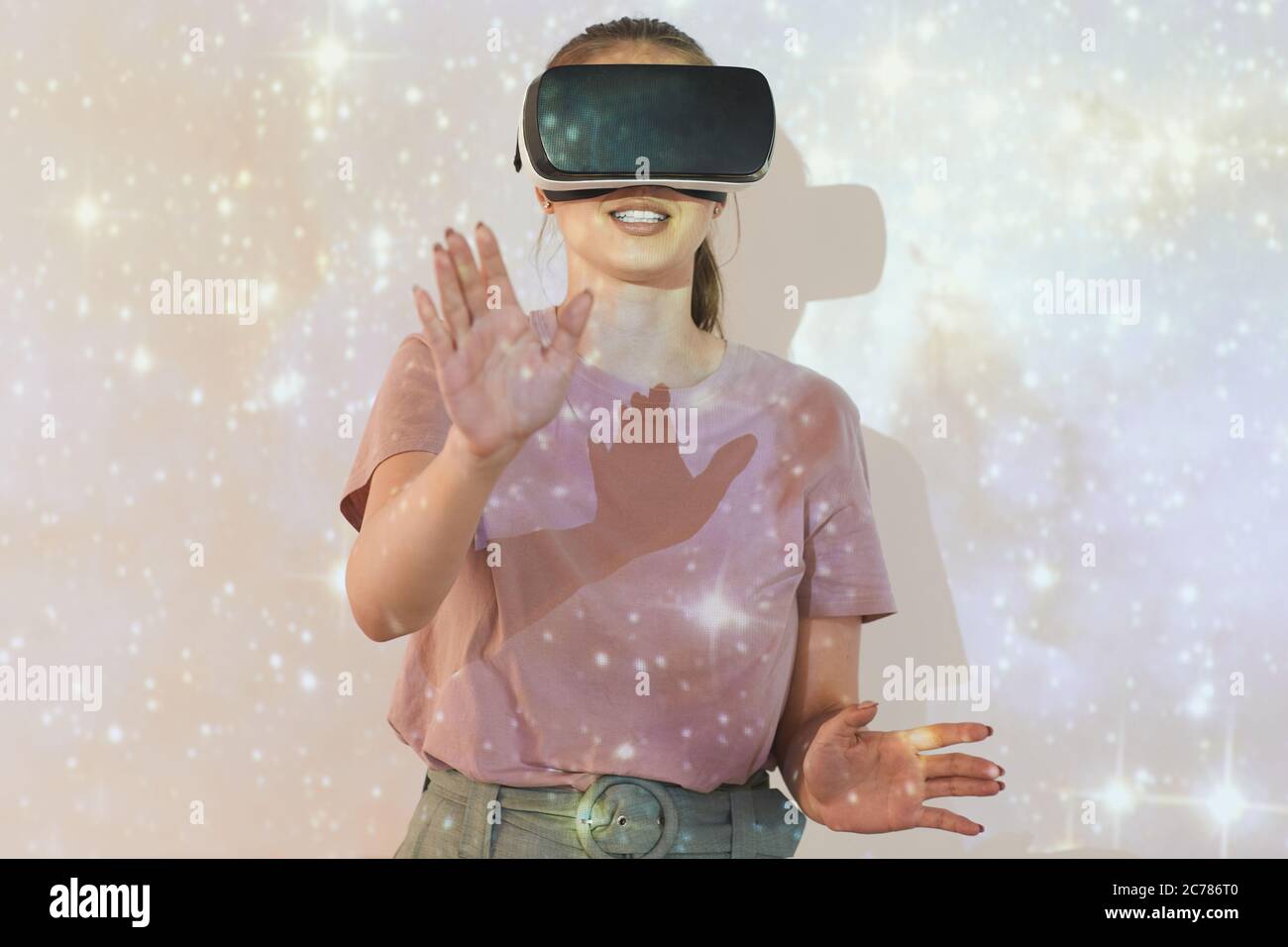 Smiling young woman standing against projection screen with glittering star sky while studying astronomy with virtual reality simulator Stock Photo