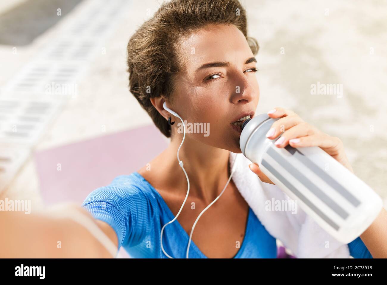 Woman in swimsuit sitting on yoga mat drinking water and taking selfie Stock Photo