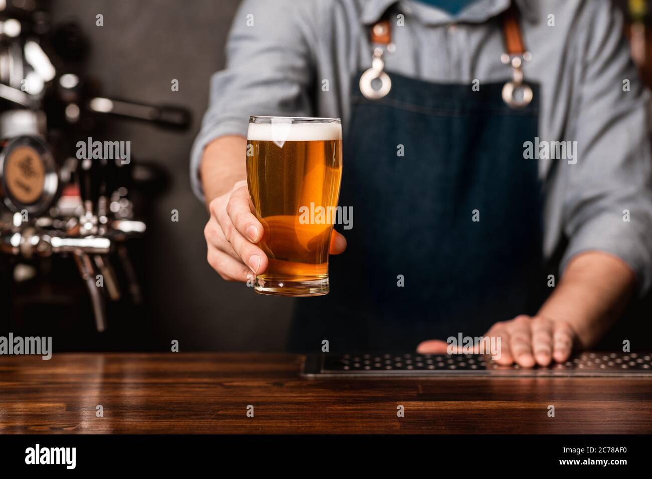 Fresh keg beer. Bartender in apron holds out a glass of light ale in interior Stock Photo