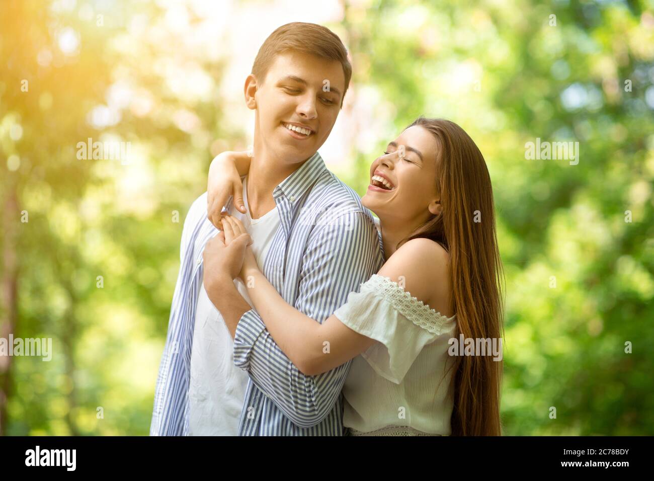 Lovely young girl laughing and hugging her handsome boyfriend at summer ...