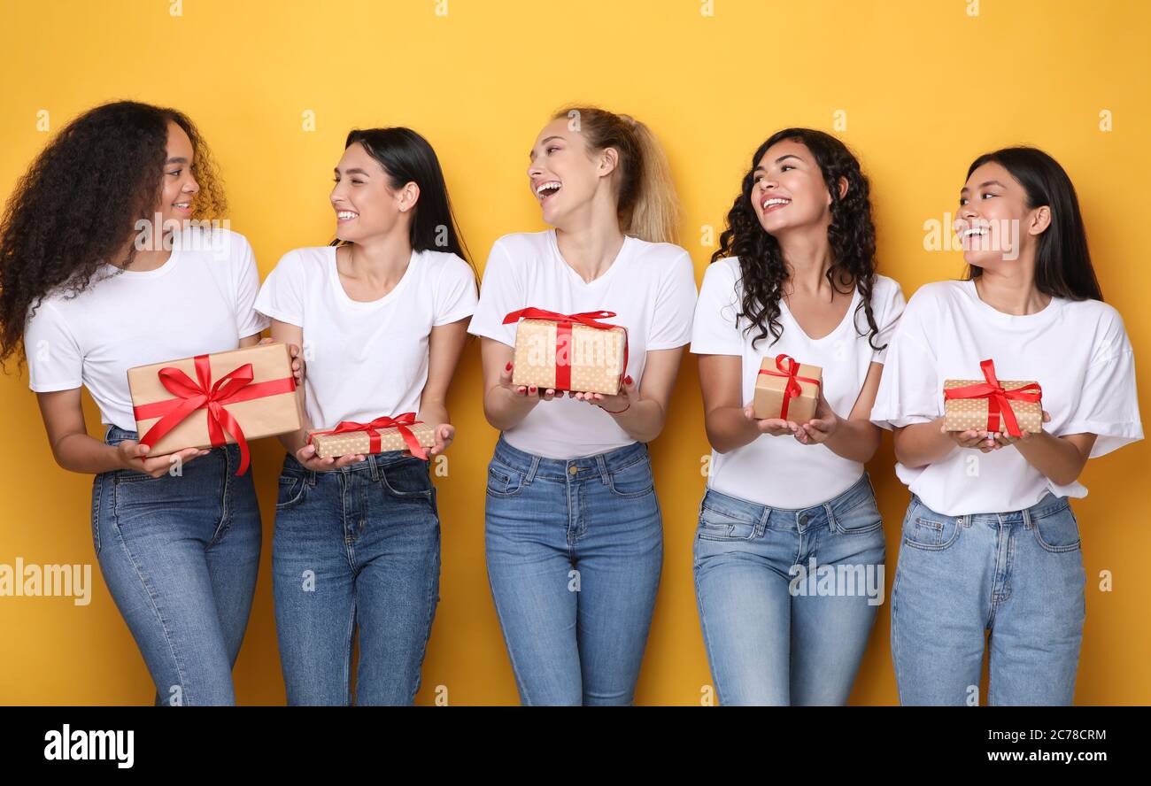 Cheerful Girls Friends Holding Wrapped Gifts Boxes Over Yellow Background Stock Photo