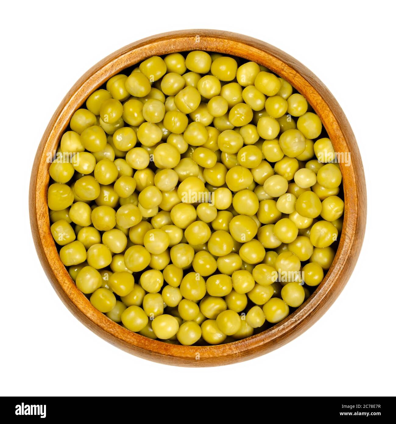 Canned green peas in wooden bowl. Small spherical seeds of the pod fruit Pisum sativum, boiled and canned to preserve the legumes. Closeup from above. Stock Photo