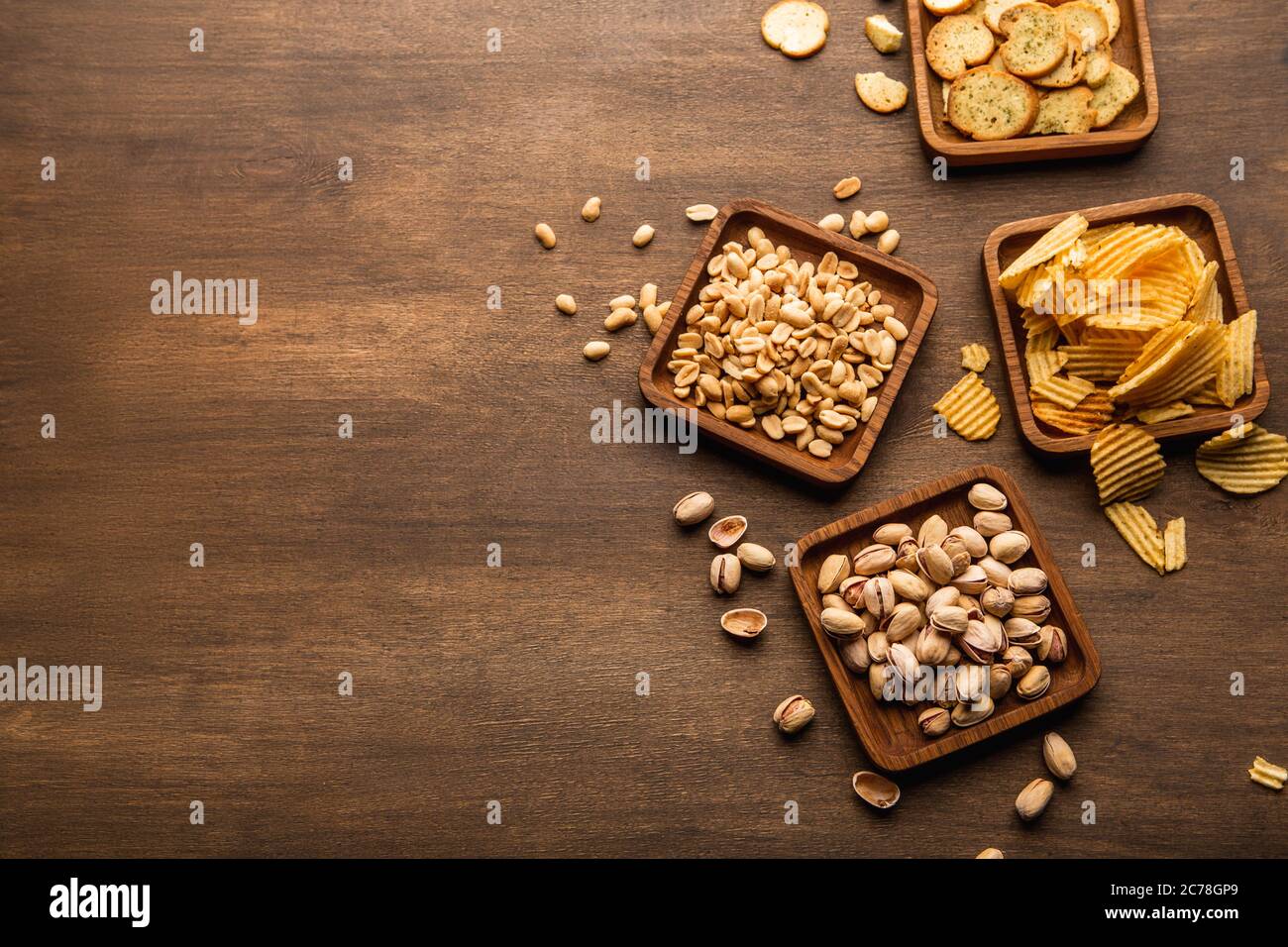 Crispy snacks on background. Pistachios, nuts, crisps and chips in plate and scattered on table Stock Photo