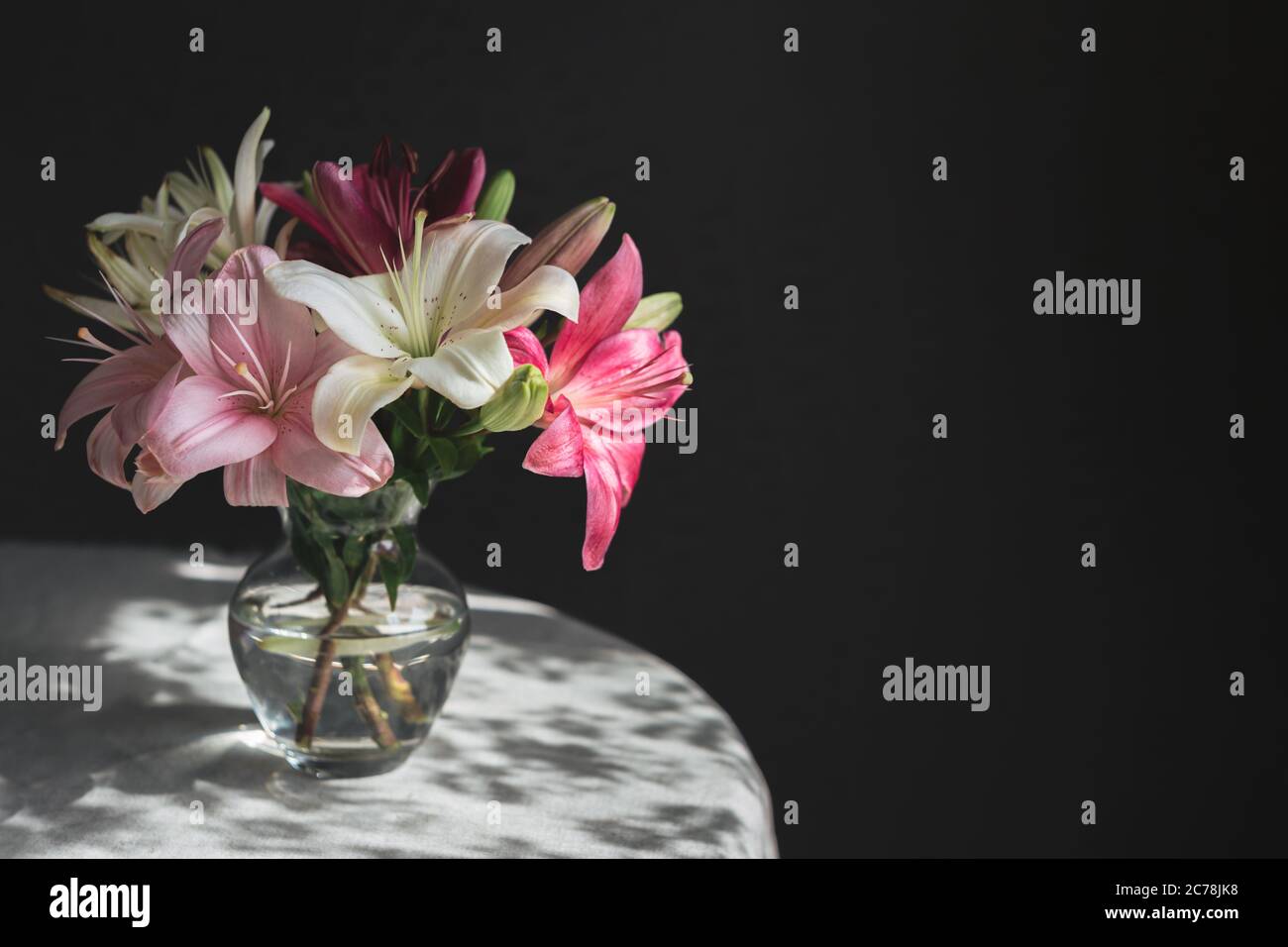 Romantic bouquet of the white and pink lilies in a glass vase on a dark ...