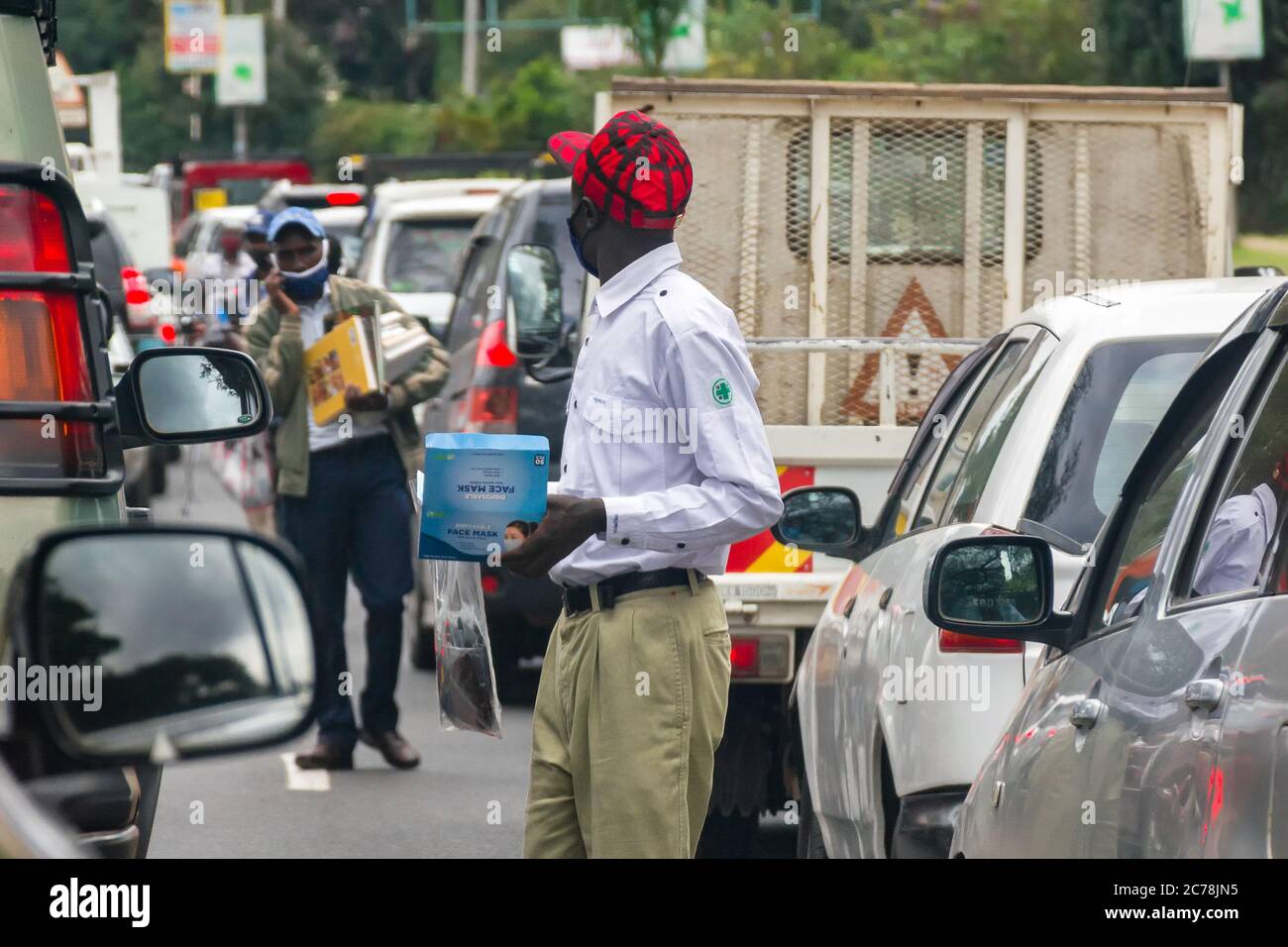 A street hawker wearing a face mask walks past vehicles stuck in traffic selling face masks, Nairobi, Kenya Stock Photo