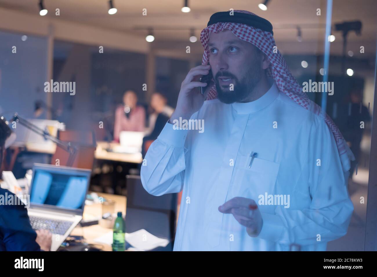 Middle Eastern businessman talking on the phone and looking out the window in his office. Businessman Arabic using mobile phone for connection to comm Stock Photo