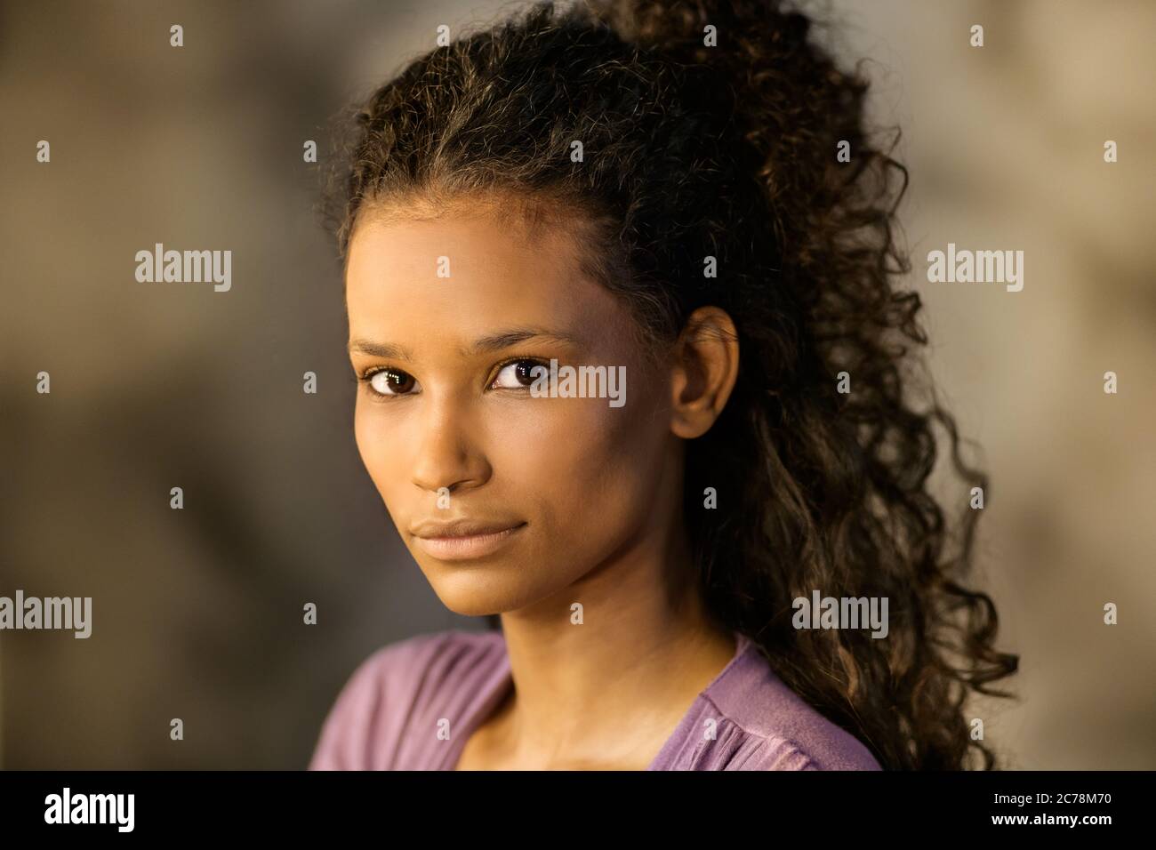 Young thoughtful Afro-american girl with long curly hair in her twenties turning to looking at the camera with a serious expression Stock Photo