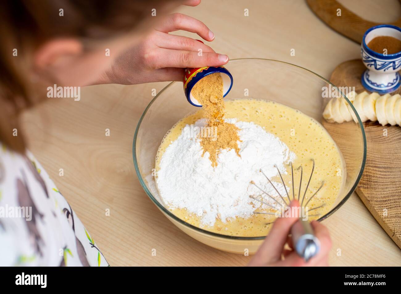 Young girl is adding spices and flour to blended bananas. Preparing easy to make and healthy, home made banana bread. Stock Photo