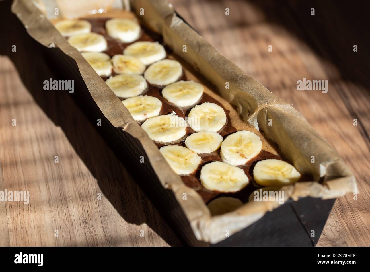 Baking form filled with banana bread dough. Cutted banana on top. Stock Photo