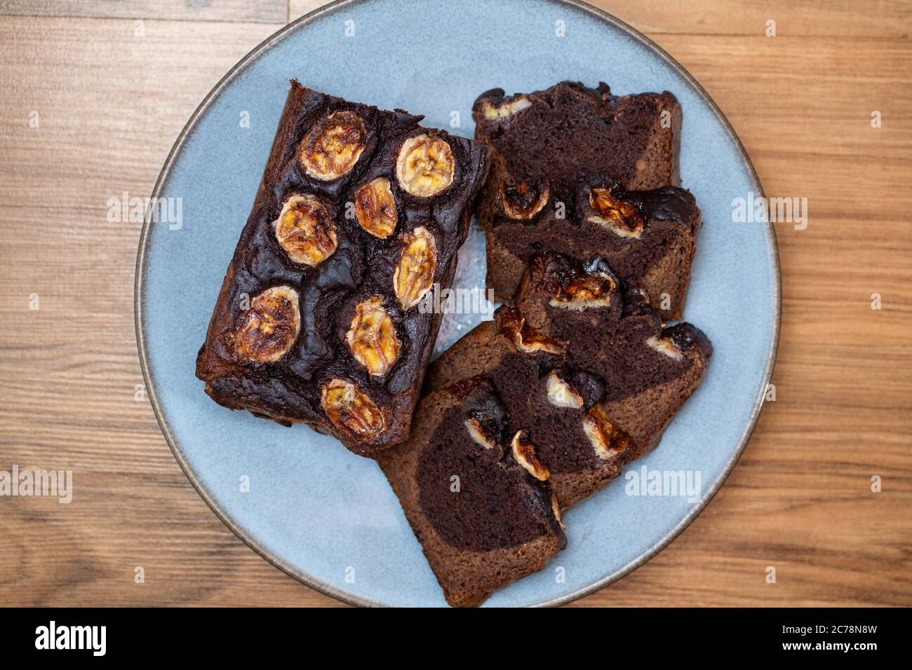 Homemade banana bread cut into slices on a blue plate. Cutted banana on top. Easy to prepare and healthy, home made pastry. Stock Photo