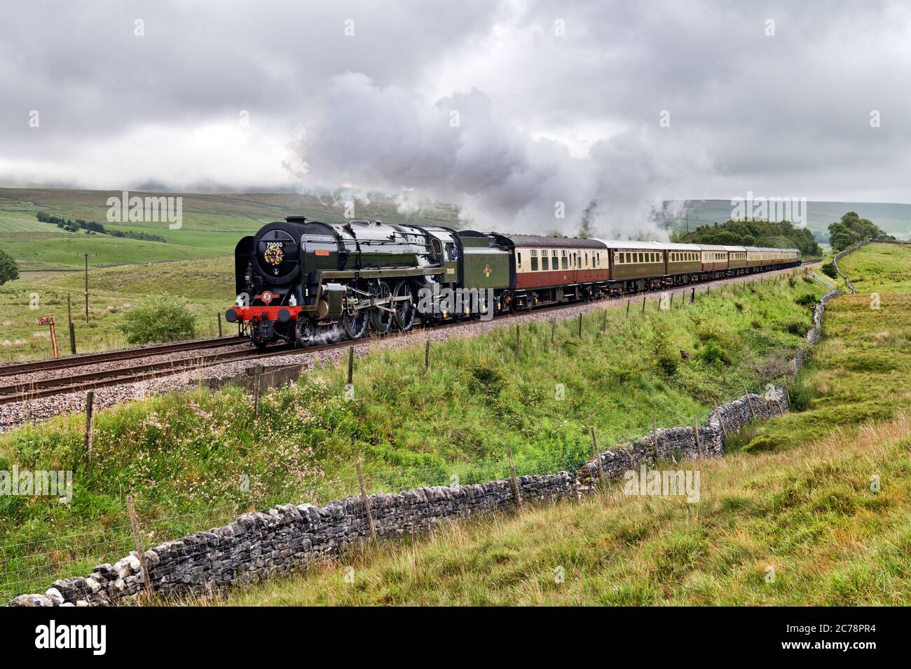 Ribblesdale, North Yorkshire, UK. 15th July 2020. Steam returns to the famous Settle-Carlisle railway line for the first time since Covid-19 lockdown began in March. Under stormy skies, iconic vintage steam locomotive 'Britannia' is seen here hauling 'The Fellsman' special train north from Settle towards Carlisle, on a trip that began at Crewe. Pictured here at Selside, Ribblesdale, in The Yorkshire Dales National Park. The service is operated by Saphos Trains. Credit: John Bentley/Alamy Live News Stock Photo