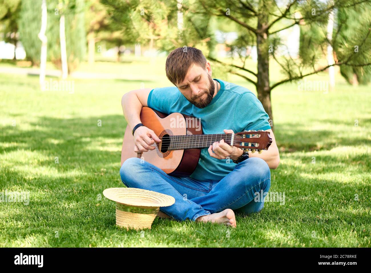 A young man plays the guitar in the park on green grass. Stock Photo