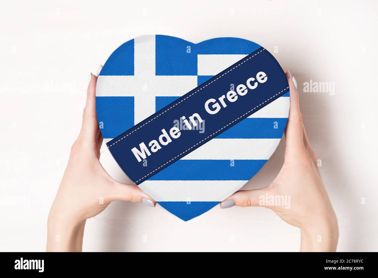 Inscription Made in Greece, the flag of Greece. Female hands holding a heart shaped box. White background. Stock Photo