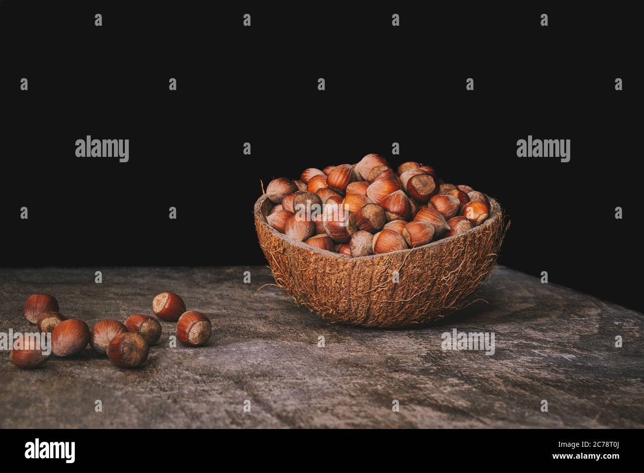 Pile of shelled hazelnuts in a coconut shell bowl on a wooden table on black background. Healthy eating. Stock Photo