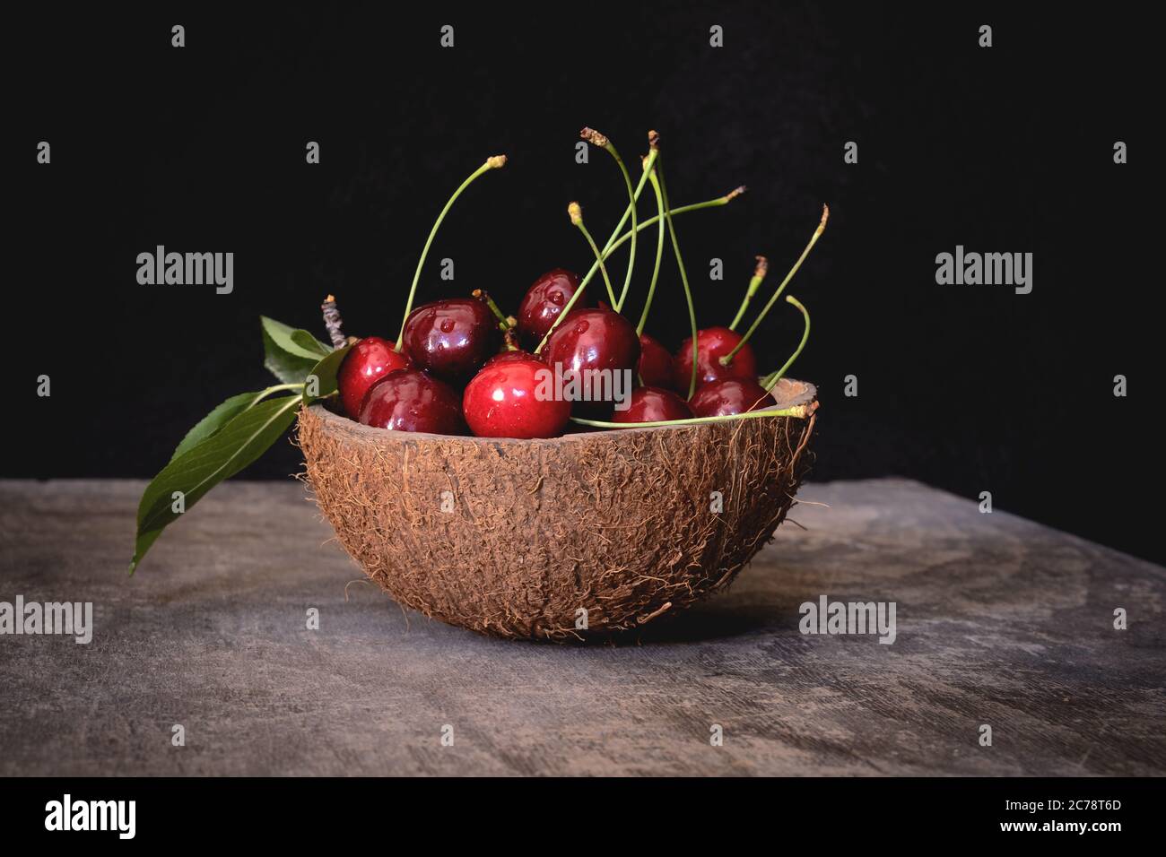 Fresh cherries in a coconut shell bowl on a wooden table on black background. Healthy eating. Stock Photo