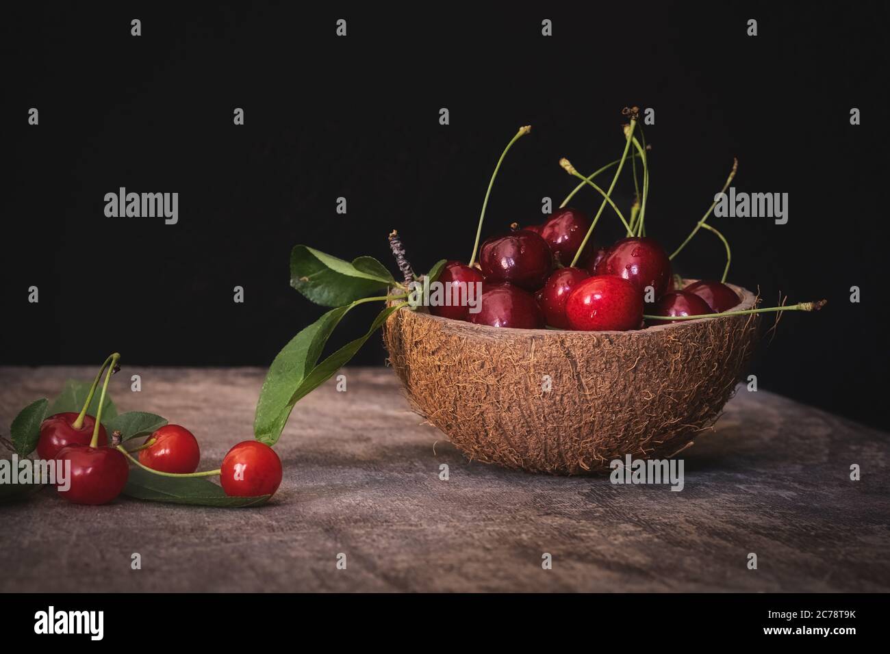 Fresh cherries in a coconut shell bowl on a wooden table on black background. Healthy eating. Stock Photo