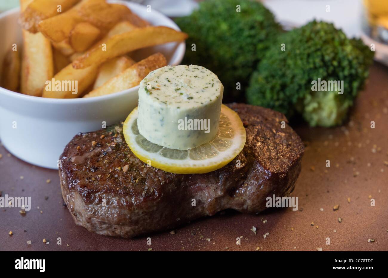 closeup of a roasted steak with herb butter, broccoli and fries served on a plate with salt and pepper Stock Photo