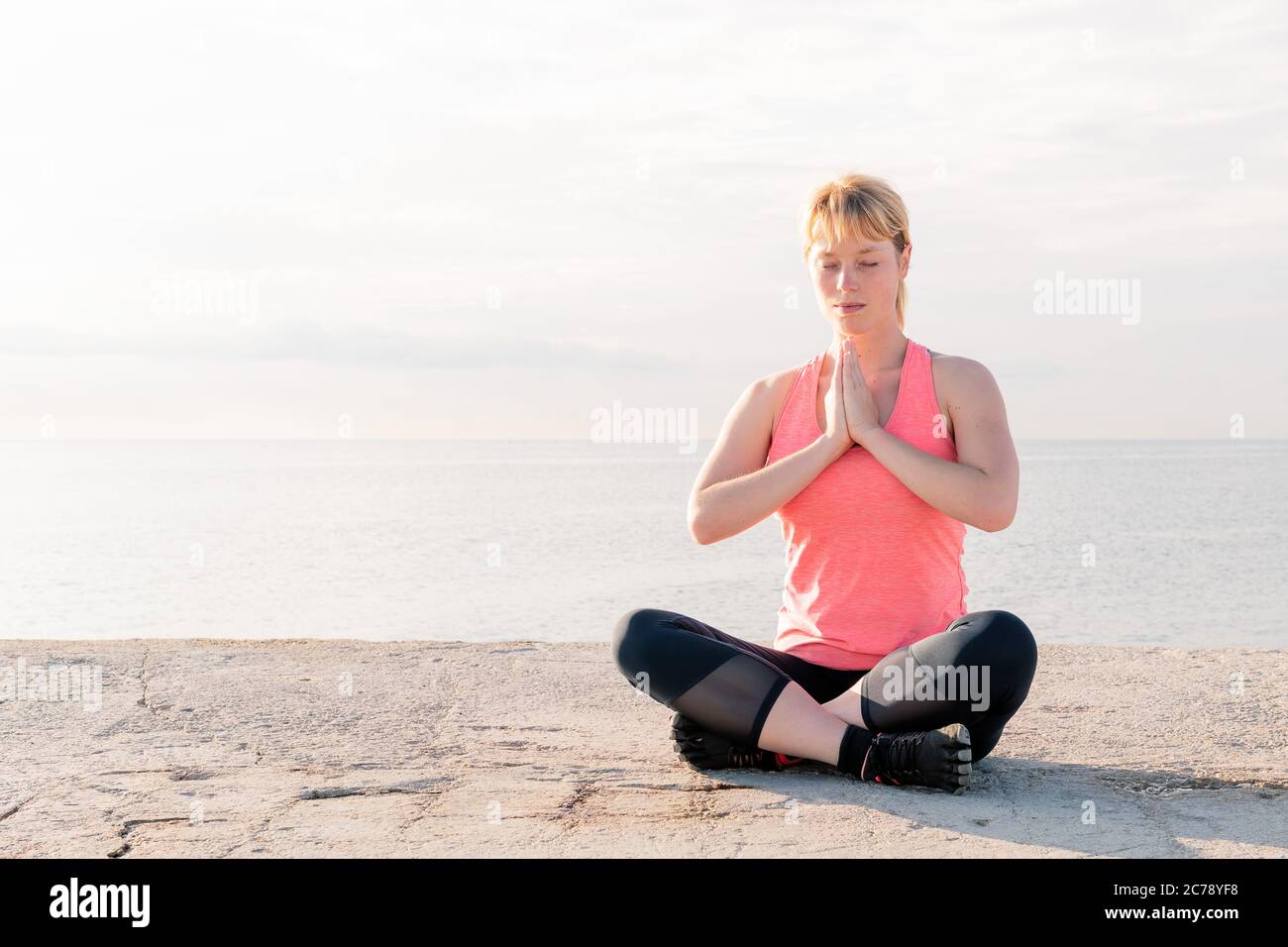 beautiful blonde woman practicing yoga at dawn sitting in front of the sea, concept of mental health and relaxation, copy space for text Stock Photo