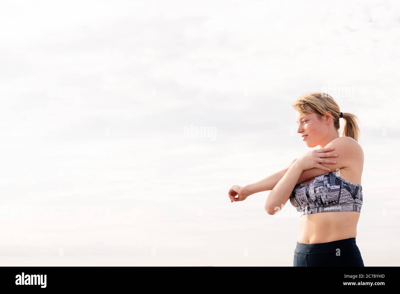 beautiful blonde sportswoman stretching with the sky in the background at dawn, healthy lifestyle and sports concept, copy space for text Stock Photo