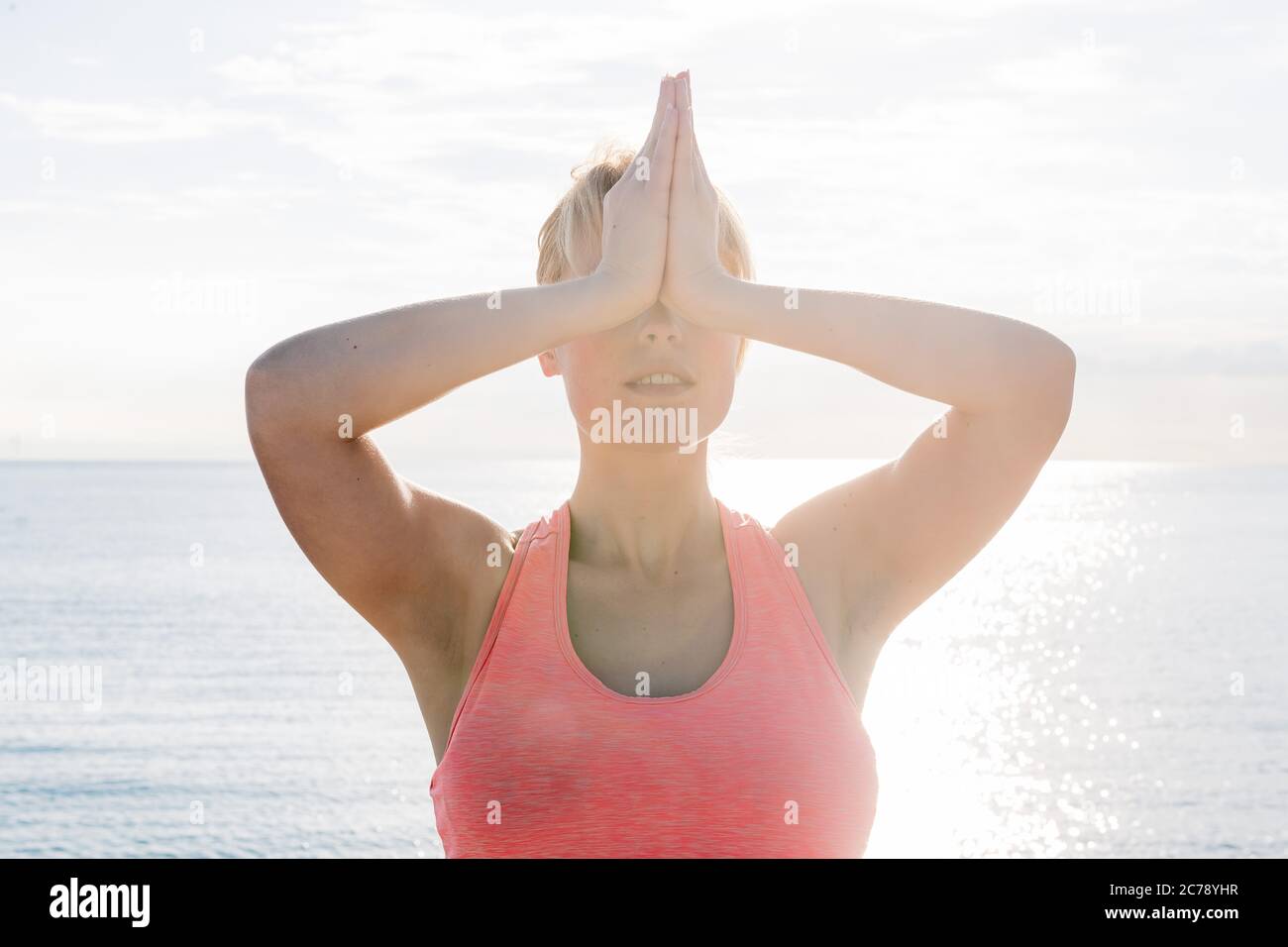 portrait of a blonde woman meditating and practicing yoga at dawn in front of the sea, concept of mental health care and relaxation Stock Photo
