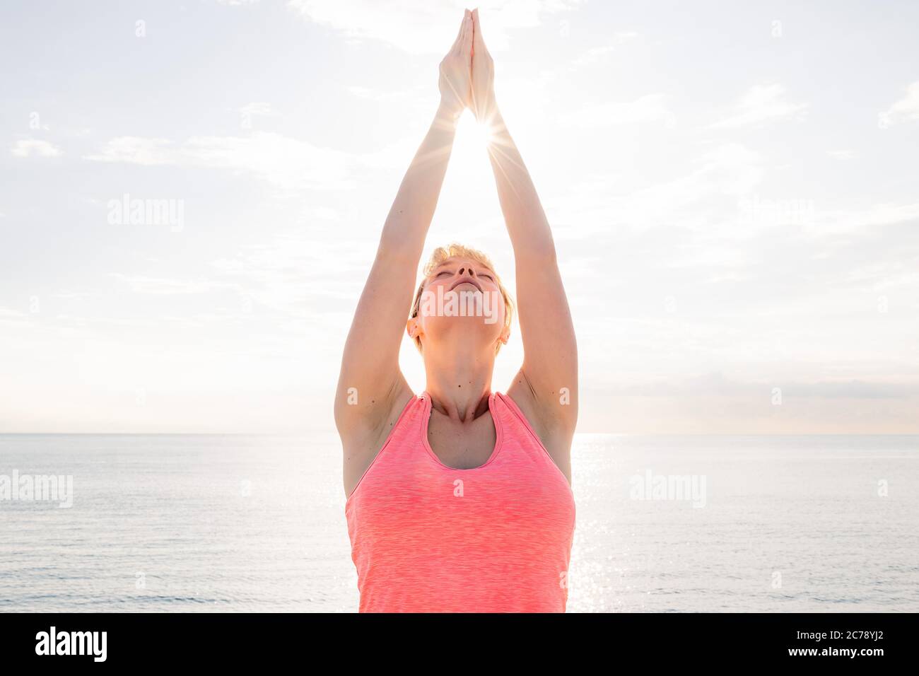 blonde woman meditating and practicing yoga at sunrise in front of the sea, concept of mental health care and relaxation, copy space for text Stock Photo