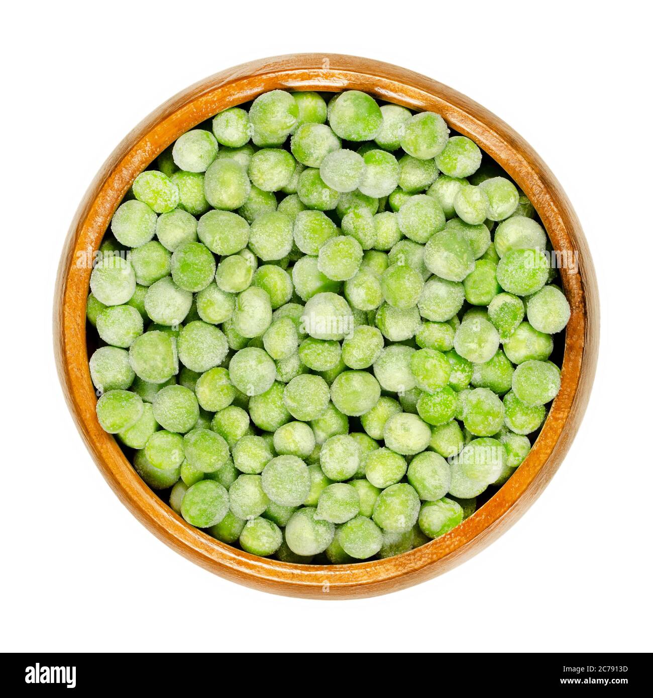 Frozen green peas in wooden bowl. Small spherical seeds of the pod fruit Pisum sativum, frozen to keep the legumes fresh. Closeup, from above. Stock Photo