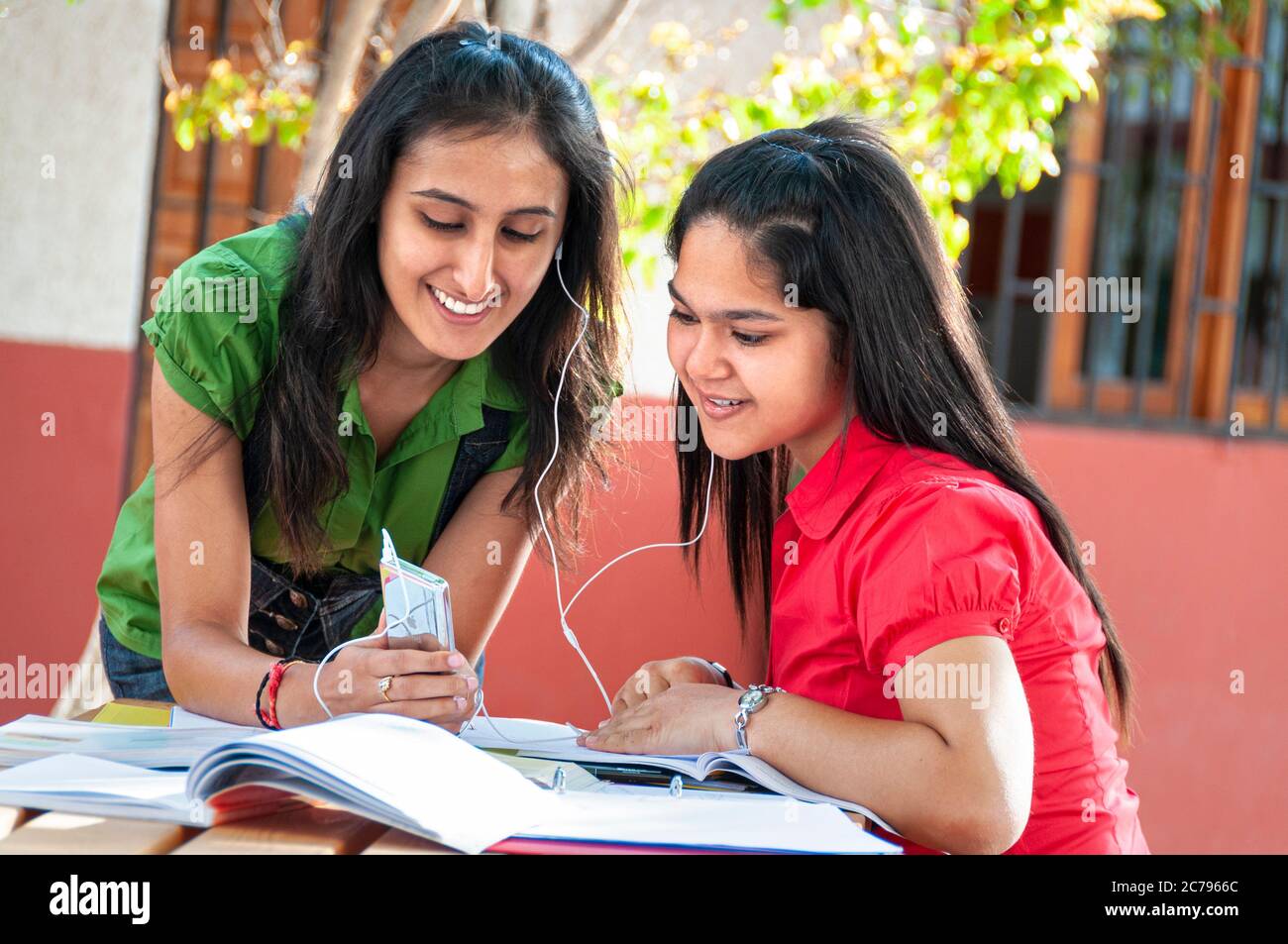 School teenage girl asian students 15-17 years sharing earphones with their Mp4 iPod player during studies outside in sunny school playground campus Stock Photo