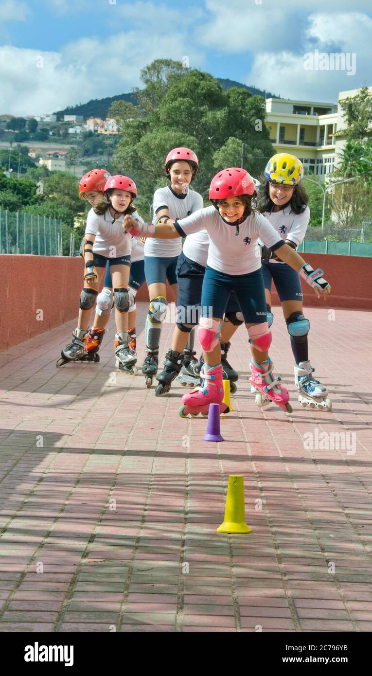 SCHOOL SPORTS JUNIORS GIRLS 9-11 years FUN ROLLERBLADE ROLLER SKATE MULTICULTURAL SPORTS TEAM OUTDOORS HAPPY Junior school girls in playground during rollerblade team slalom game wearing full rollerblade safety clothing including knee protectors & helmets Stock Photo
