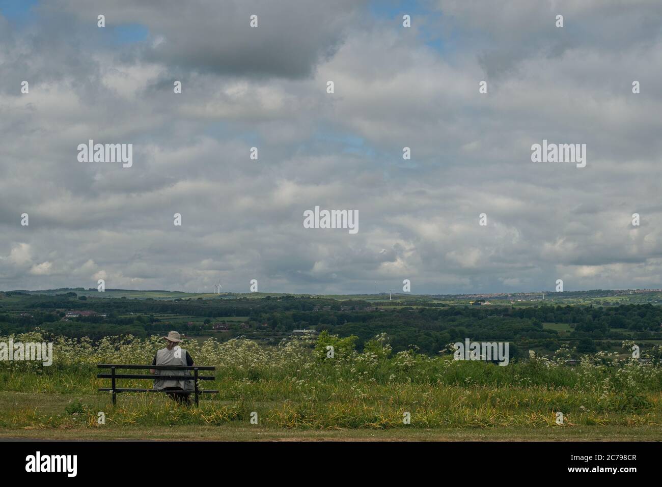 Single seated figure on a bench overlooking the countryside and enjoying the view Stock Photo