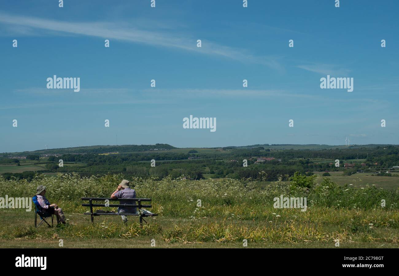 two figures, seated and in conversation, enjoying a quiet sunny day overlooking the countryside while maintaining social distancing Stock Photo
