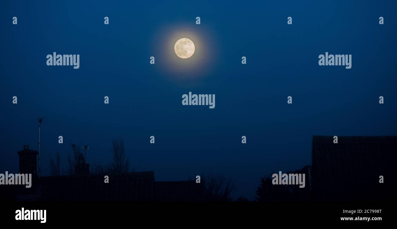 Moon rise with moon glow over domestic buildings and dark blue sky Stock Photo