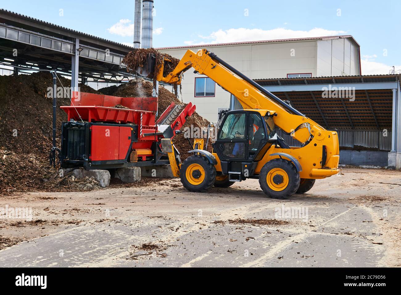 bucket loader loads wood bark into an industrial woodchipper in a woodworking industry Stock Photo