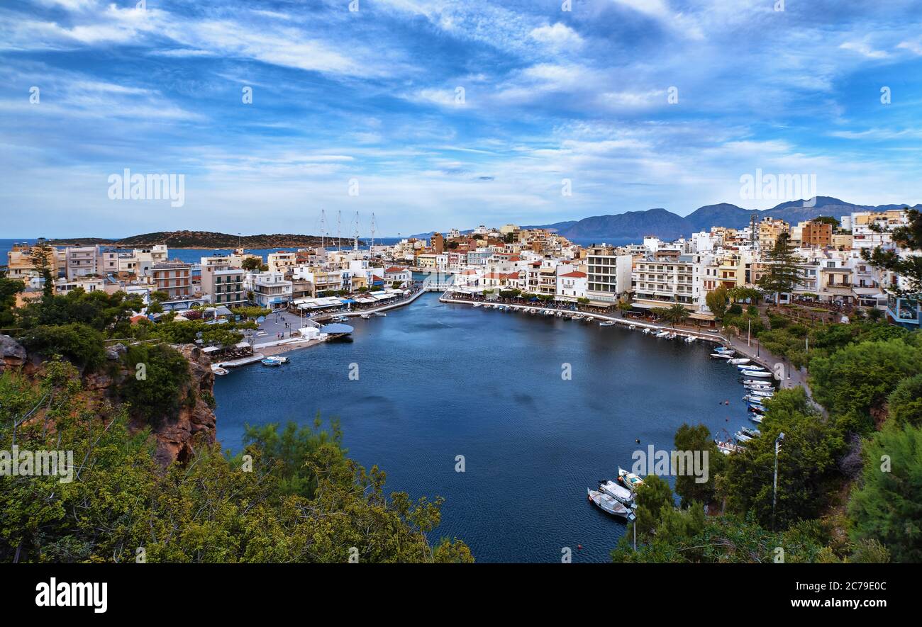 Colorful view of Voulismeni lake and Agios Nikolaos town on Crete island, Greece in evening with beautiful clouds on blue sky. Stock Photo
