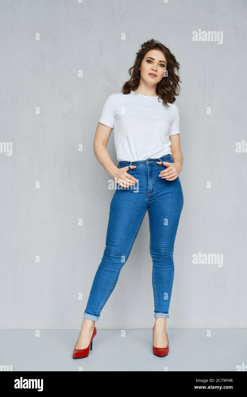 Positive girl in jeans, white t-shirt and red stilettos posing near the  wall holding hands in the pockets Stock Photo - Alamy